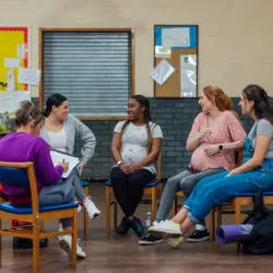 A wide angle view of a group of women at a female led maternity antenatal class in a community centre in the North East of England. They are sat in a circle and finding out about the fitness classes available to them.